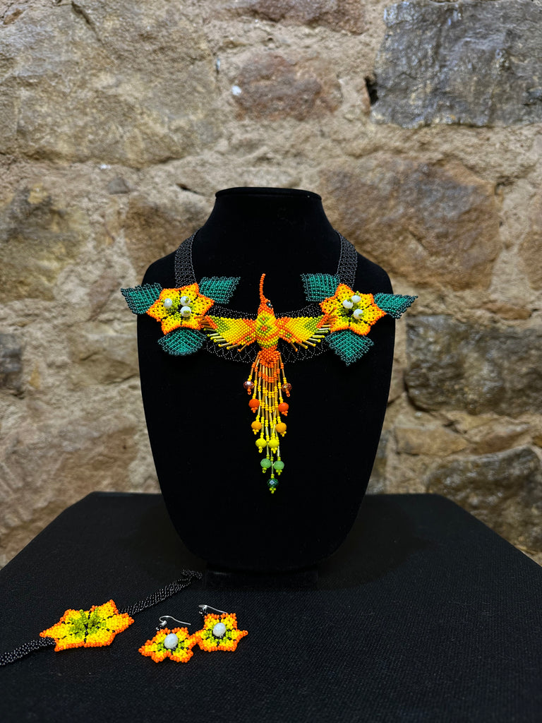 This vibrant hummingbird necklace and earring set are sure to bring a touch of cheerful color to any look. Expertly crafted, each set is made up of three-dimensional beading of flower set among three leaves with a 6
