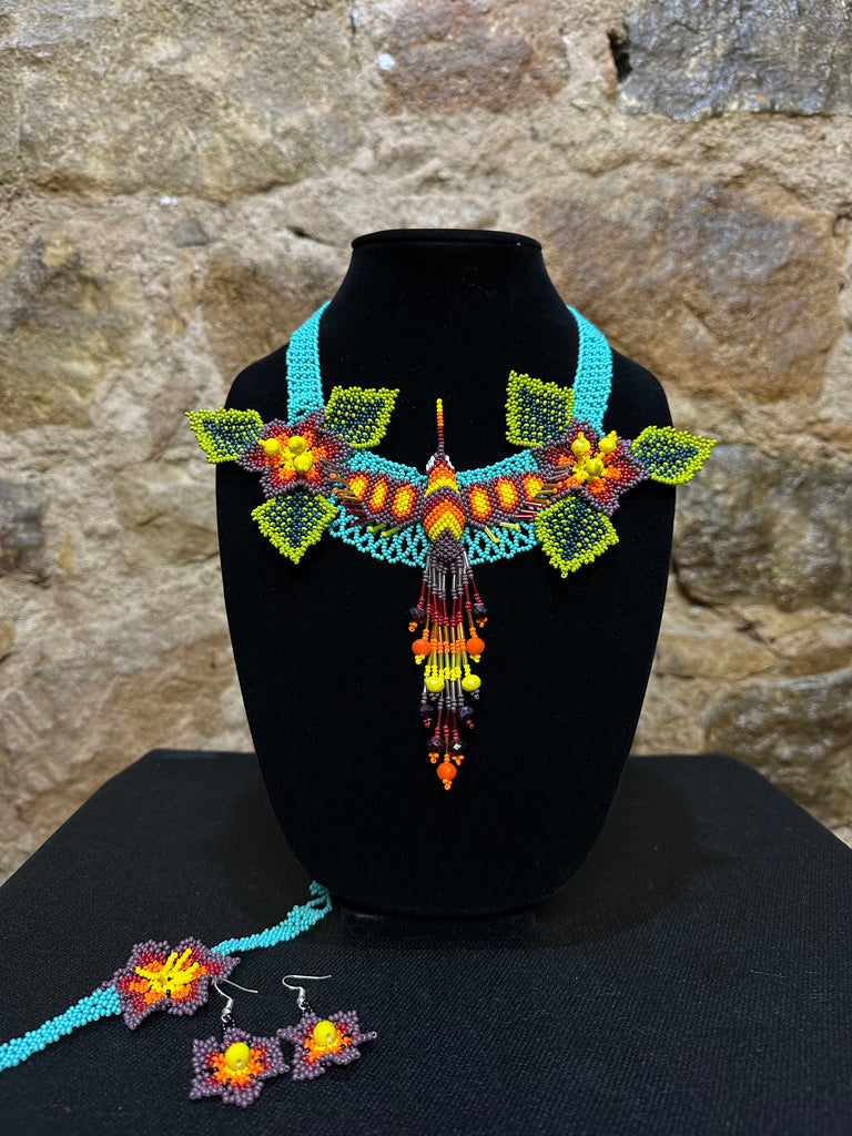 This vibrant hummingbird necklace and earring set are sure to bring a touch of cheerful color to any look. Expertly crafted, each set is made up of three-dimensional beading of flower set among three leaves with a 6